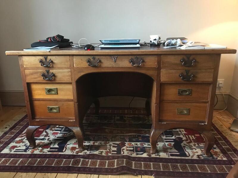 Antique oak pedestal desk with ornate brass and iron handles on Persian rug before restoration