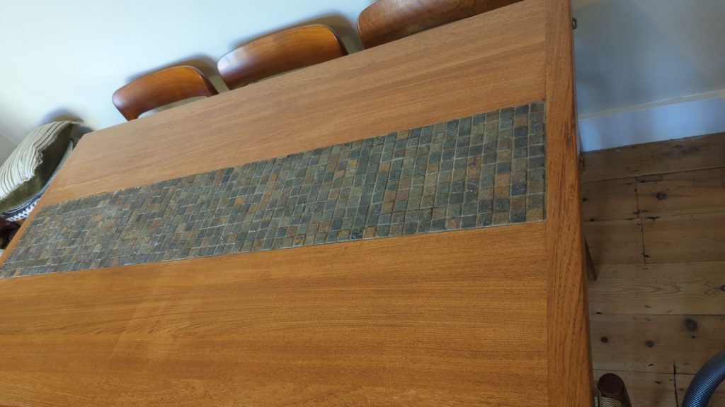 Close-up of mid-century teak dining table surface with slate mosaic tile inlay strip