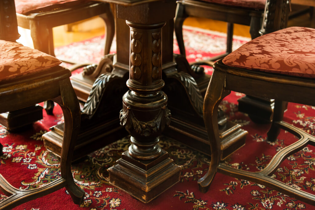 Antique dark wood dining table with ornate carved pedestal leg and red damask upholstered chairs